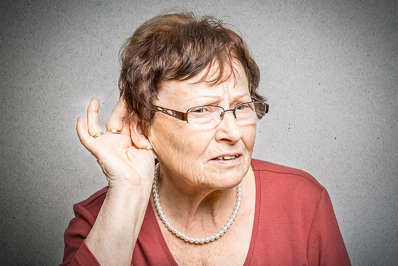 Frau hält sich die Hand ans Ohr um zu signalisieren, dass sie schwer hören kann.