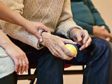 Pflegende unterstützt Patienten dabei einen Ball zu greifen.