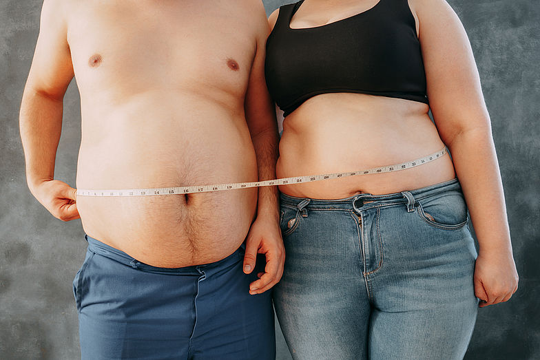 Zwei oberkörperfreie Personen, die ihren Fortschritt messen: Symbolisches Maßband um den Körper beider Personen, welches die Gesundheitsziele widerspiegelt