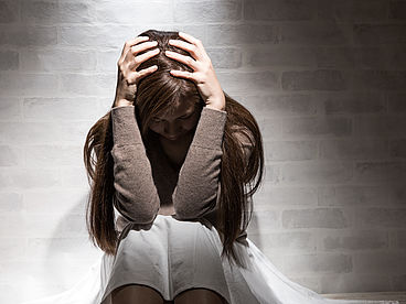 Frau mit einer somatoformen Störung hockt vor einer Wand und hält die Hände am Kopf.